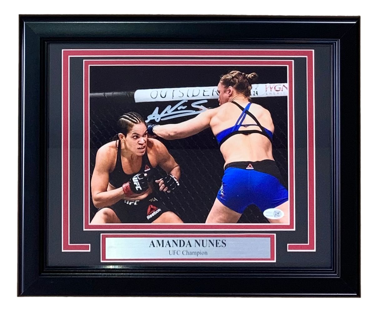 Sports Integrity Amanda Nunes Signed Framed 8x10 UFC Rousey Fight Photo features two female MMA fighters in the octagon, Nunes throwing a punch, with a “AMANDA NUNES UFC Champion” plaque and her white signature above. JSA QR Hologram included.