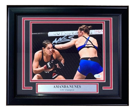 Sports Integrity Amanda Nunes Signed Framed 8x10 UFC Rousey Fight Photo features two female MMA fighters in the octagon, Nunes throwing a punch, with a “AMANDA NUNES UFC Champion” plaque and her white signature above. JSA QR Hologram included.