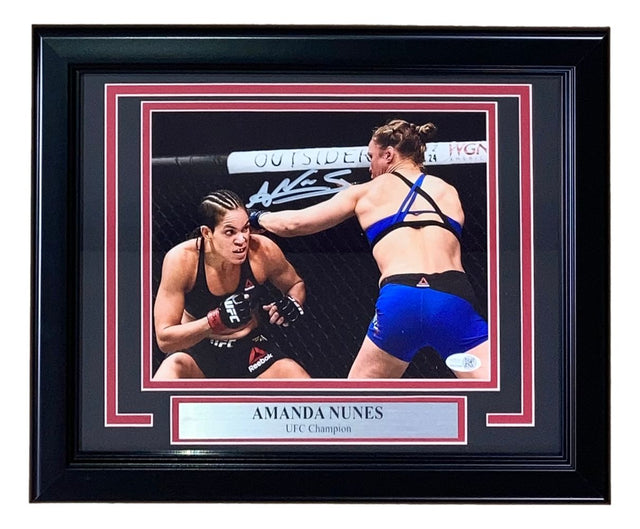 Sports Integrity Amanda Nunes Signed Framed 8x10 UFC Rousey Fight Photo features two female MMA fighters in the octagon, Nunes throwing a punch, with a “AMANDA NUNES UFC Champion” plaque and her white signature above. JSA QR Hologram included.