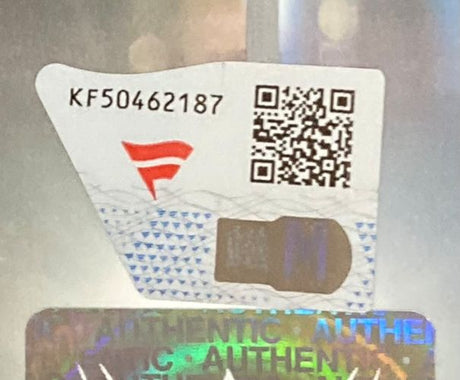 A close-up of a Sports Integrity security label for the Austin Theory Signed Framed 8x10 WWE Photo Fanatics, featuring code KF50462187, a red logo, QR code, and a holographic sticker with "AUTHENTIC" partially visible.