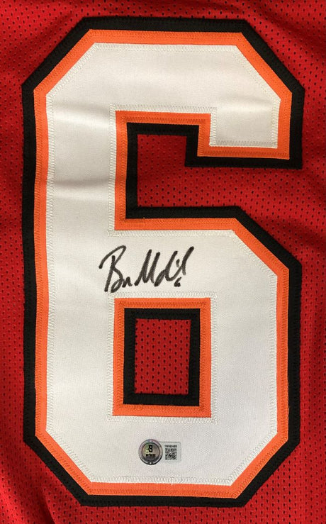 A large white and orange number 6 is printed on a red Baker Mayfield Tampa Bay football jersey. Signed in black marker with an authentication sticker, this jersey is offered by Sports Integrity and authenticated by BAS.