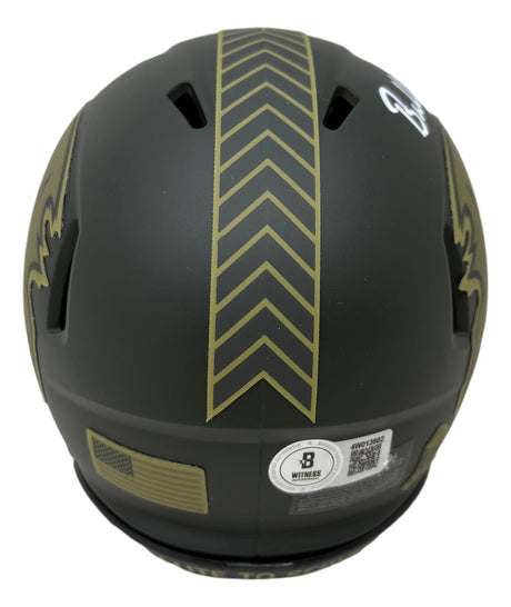 A Baker Mayfield Signed Buccaneers Salute To Service Mini Speed Helmet by Sports Integrity, black with gold chevron stripes and a fleur-de-lis design, viewed from the back with stickers including a QR code and certification label.