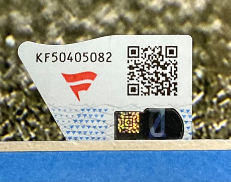 A close-up of a security sticker on a Sports Integrity Bryce Young Signed Framed 16x20 Carolina Panthers Photo Fanatics, showing KF50405082, a red logo, QR code, hologram, and part of the blue and white background.