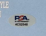 Close-up of the PSA/DNA hologram sticker with code 4C52548 on the Charlie Sheen Signed 11x17 Major League Photo by Sports Integrity, featuring the PSA logo and "IN-THE-PRESENCE™" text on a light blue background.