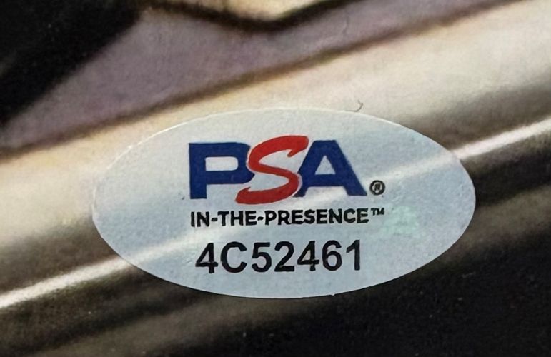 Oval sticker with PSA IN-THE-PRESENCE™ 4C52461 printed on it, featuring PSA's blue and red logo on a light background. Comes with the Sports Integrity Charlie Sheen Signed 11x14 Wall Street Photo and a PSA/DNA hologram.