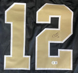 The Sports Integrity Chris Olave New Orleans Signed Black Football Jersey features large gold and white number 12, with Olave's signature in black marker on the "2" and a BAS authentication sticker below it.