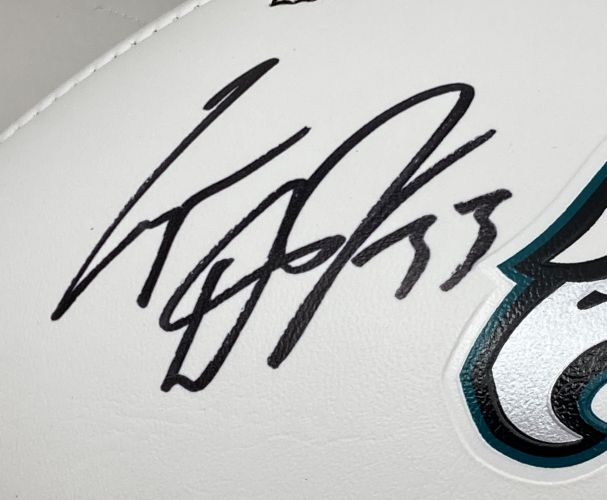 A close-up of a Cooper Dejean signed Eagles logo football from Sports Integrity, featuring a large black autograph near the teal and black logo, displayed in a Fanatics Super Bowl 59 LIX case.