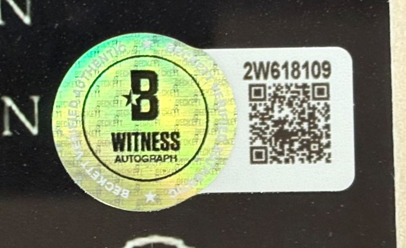 A holographic Beckett Witness Autograph sticker with QR code and ID 2W618109 is affixed to the Sports Integrity Corey Feldman Signed Framed 11x17 The Lost Boys Photo Peace Inscribed BAS, featuring the Beckett logo, "Witness," and security patterns.