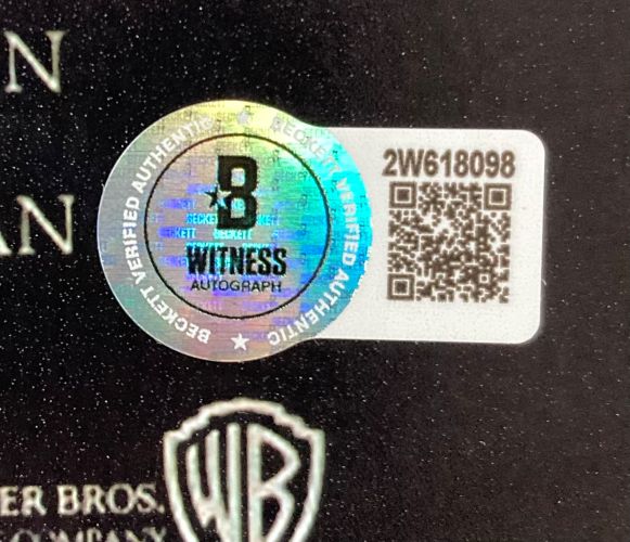 A holographic Beckett Witness Autograph sticker labeled “2W618098” with a QR code is affixed to a Sports Integrity Corey Feldman Signed 11x17 The Lost Boys Photo Peace Inscribed BAS, partially above a white and gold Warner Bros. logo.
