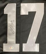 A large white number 17, signed in black marker and featuring an authentication sticker, is stitched onto the black mesh of the Davante Adams Oakland Signed Black Football Jersey by Sports Integrity.