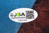 A white oval JSA Authenticated sticker with holographic logo, QR code, and ID CI84194 is affixed to the Matthew De Merritt Signed 11x14 ET Photo by Sports Integrity on a blue and brown background.