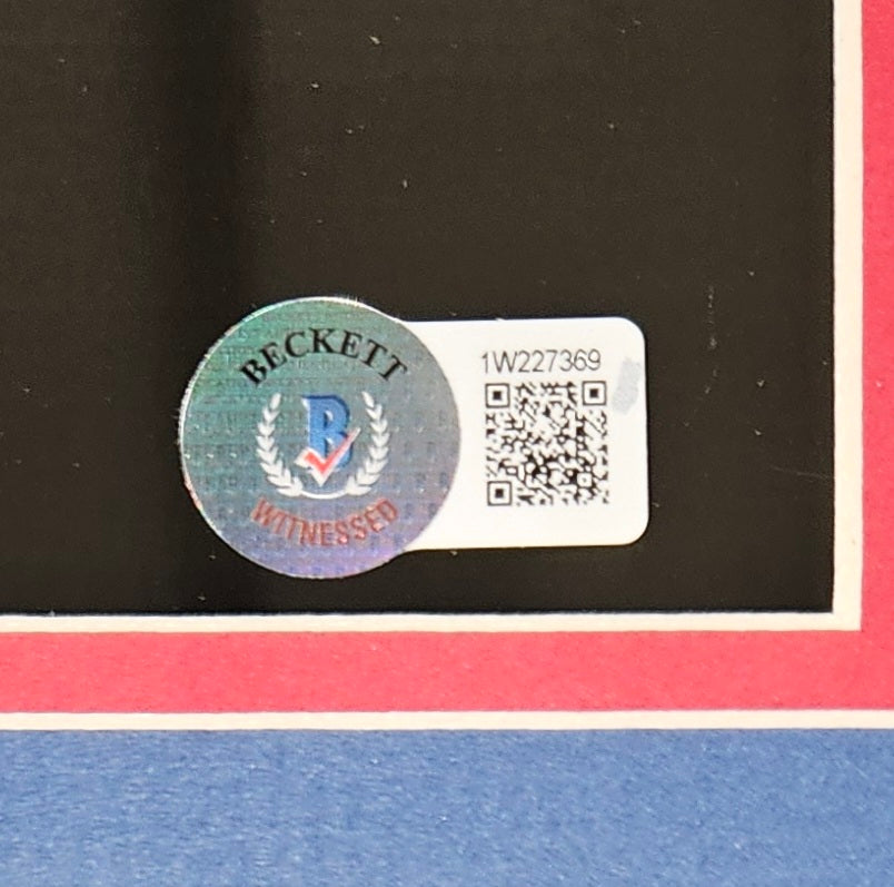 A close-up of a Beckett Witnessed holographic sticker and barcode label (code 1W227369) on the Sports Integrity Tommy Devito Signed Framed 11x14 New York Giants Spotlight Photo BAS ITP, with a black background bordered in red and white.