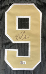 A gold and white number 9 is sewn onto black mesh fabric on this Drew Brees New Orleans Signed Black Football Jersey by Sports Integrity, featuring his signature in black ink and an authentication sticker at the bottom.