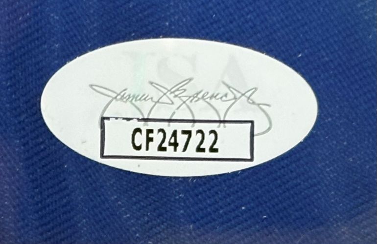 An oval authentication sticker with code CF24722 in bold black on white appears on the blue textured Sports Integrity Dustin Johnson Signed Framed 2025 PGA Championship Golf Flag JSA. A faint signature is visible in the background.