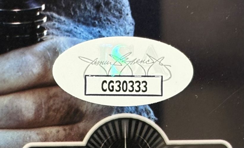 A close-up of an oval JSA sticker with code CG30333 on a white background, partially covering Ewan McGregor’s signature on a Sports Integrity 8x10 framed Star Wars Obi-Wan Kenobi photo, with part of a hand holding a metallic object behind it.