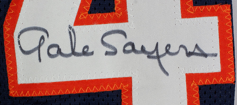 Close-up of a Gale Sayers signature in black ink on a white patch with orange trim, stitched onto a navy blue Sports Integrity custom blue pro style football jersey, authenticated by PSA/DNA.