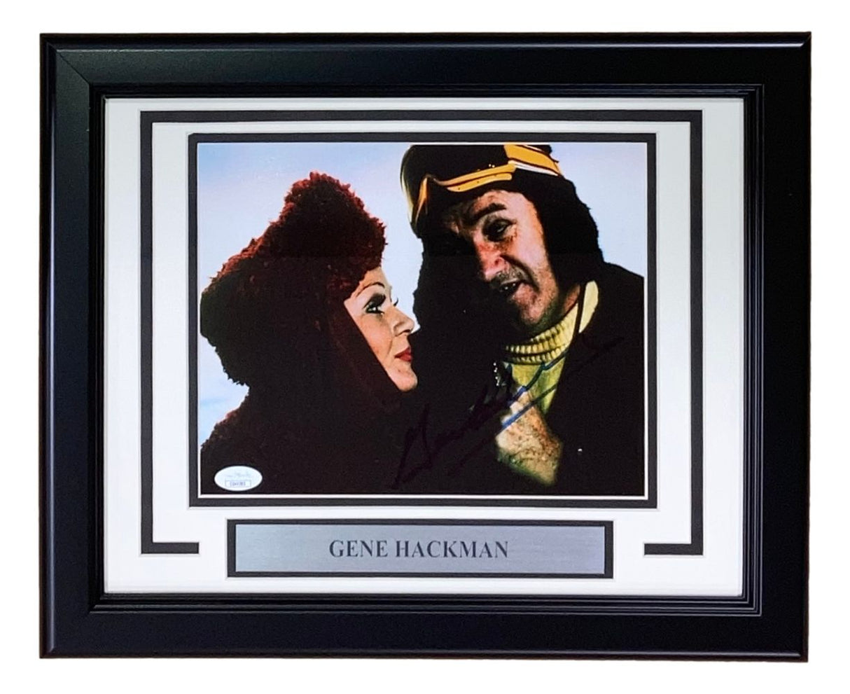 Sports Integrity's Gene Hackman Signed Framed 8x10 Superman II Photo features two costumed characters, one in a red hood and one in a yellow and brown headpiece. Includes a plaque with Gene Hackman's name. Authenticated by JSA.