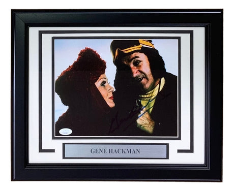 Sports Integrity's Gene Hackman Signed Framed 8x10 Superman II Photo features two costumed characters, one in a red hood and one in a yellow and brown headpiece. Includes a plaque with Gene Hackman's name. Authenticated by JSA.