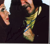 A close-up shows a red-haired woman with makeup facing a man in a yellow turtleneck, his hand visible, on this Gene Hackman Signed Framed 8x10 Superman II Photo by Sports Integrity, featuring a bold autograph across the image.