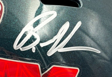 A close-up of the Brandon Graham Signed Eagles FS Super Bowl 59 LIX Replica Helmet by Sports Integrity shows a large silver autograph on its glossy, dark green surface, with part of a red and white sticker at the bottom.