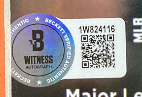 A close-up of a shiny, circular Beckett Witness Autograph sticker with QR code and serial #1W824116, attached to a Gunnar Henderson Signed Framed 16x20 Baltimore Orioles Photo by Sports Integrity. Text runs around the sticker edges.