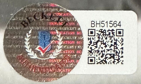 A circular holographic security sticker with a crest and check mark sits next to a white label showing BH51564 and a QR code on the metallic, reflective packaging of the Sports Integrity Hulk Hogan Signed Framed 16x20 Rocky vs Thunderlips Photo BAS.