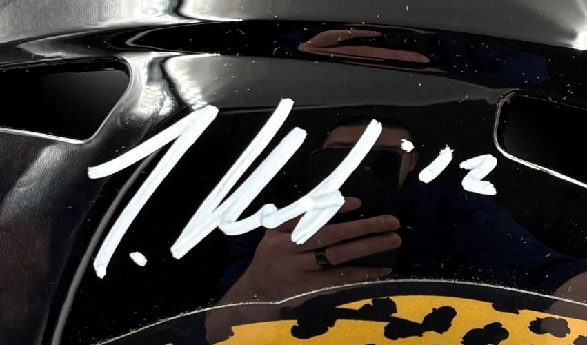 A close-up of a Travis Hunter signed Jacksonville Jaguars FS Speed Replica Helmet by Sports Integrity, featuring the number 12 and a white signature. The shiny surface reflects the person taking the photo. Includes BAS authentication and display case.