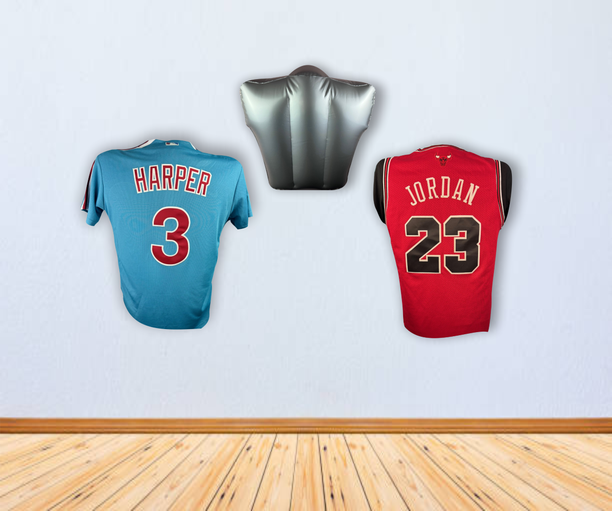 Two sports jerseys, one blue (Harper 3) and one red (Jordan 23), hang on a light wall beneath the Sports Integrity Inflatable Torso Jersey Display for Baseball and Basketball Jerseys. The floor is wooden.