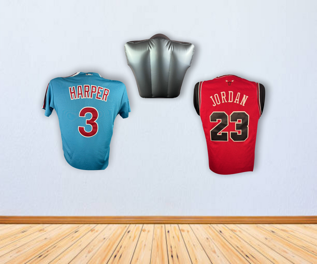 Two sports jerseys, one blue (Harper 3) and one red (Jordan 23), hang on a light wall beneath the Sports Integrity Inflatable Torso Jersey Display for Baseball and Basketball Jerseys. The floor is wooden.