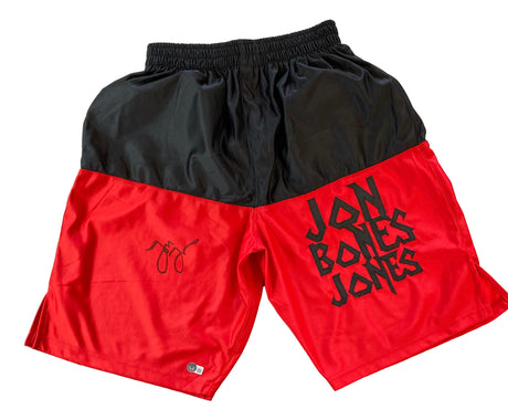 Sports Integrity’s Jon Jones Signed Custom Black/Red MMA Fighting Trunks BAS ITP are displayed on a white background, featuring bold black “JON BONES JONES” lettering on the right leg and a signature-style graphic on the left leg.