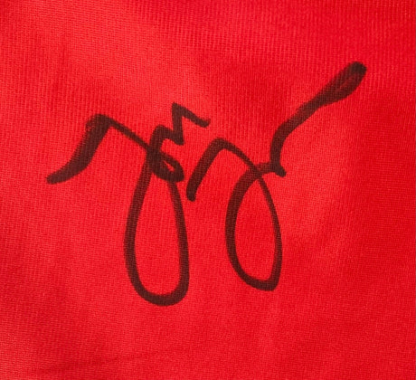 A stylized black signature with loops and curves appears on the bright red fabric of Sports Integrity's Jon Jones Signed Custom Black/Red MMA Fighting Trunks (BAS ITP), though no clear letters are visible.
