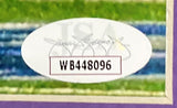 A white oval sticker with WB448096 in black appears on the Justin Tucker Signed Framed 16x20 Ravens Record Kick Photo by Sports Integrity, against a colorful blurred background. Faded text and a faint logo are also visible on the sticker.