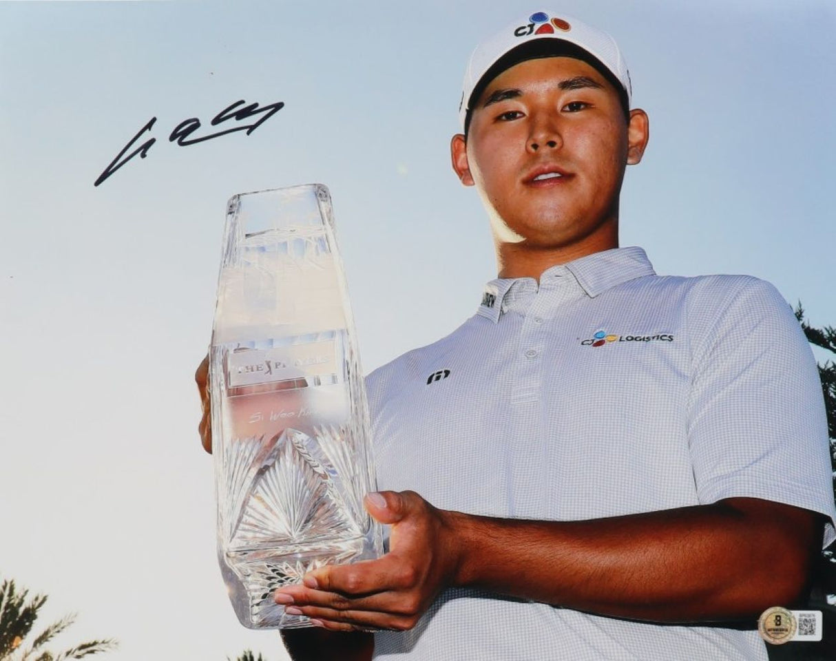 Si Woo Kim, in a white shirt and cap, holds a clear trophy in this signed 11x14 PGA Golf Photo by Sports Integrity. His signature appears in the top left. Palm trees and a blue sky enhance the background.