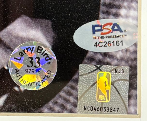 Close-up of three authentication stickers on a Sports Integrity Larry Bird Signed Framed 16x20 Celtics w/ Red Auerbach Photo: holographic Bird AUTHENTICATED, silver PSA 4C26161, and NBA logo NC046033847.