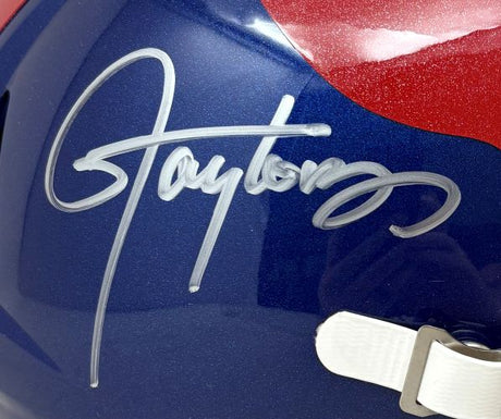 A close-up of the Lawrence Taylor Signed New York Giants FS Alternate Speed Replica Helmet by Sports Integrity, featuring a large silver autograph, white chinstrap, and part of the red design.