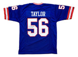 The Sports Integrity Lawrence Taylor New York signed blue football jersey features red and white sleeve stripes, "TAYLOR" and number 56 on the back, with the number autographed in black ink and JSA QR hologram authentication.