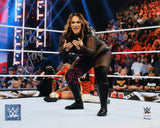 Nia Jax, in black and purple gear, poses confidently in the ring with a fallen opponent behind her and a cheering crowd, as featured in the Sports Integrity Nia Jax Signed 8x10 WWE Photo from Fanatics.
