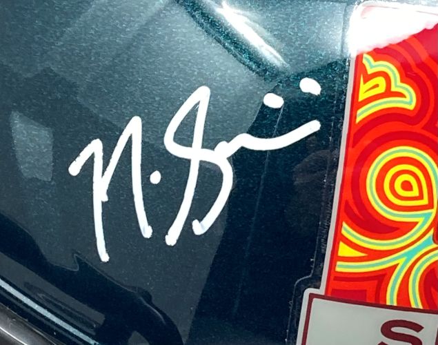 Nick Sirianni's white signature in marker appears on the glossy Sports Integrity Eagles FS Super Bowl 59 LIX Replica Helmet, displayed next to a vibrant sticker with red, orange, and yellow swirls. Reflections show on the shiny helmet and included display case.