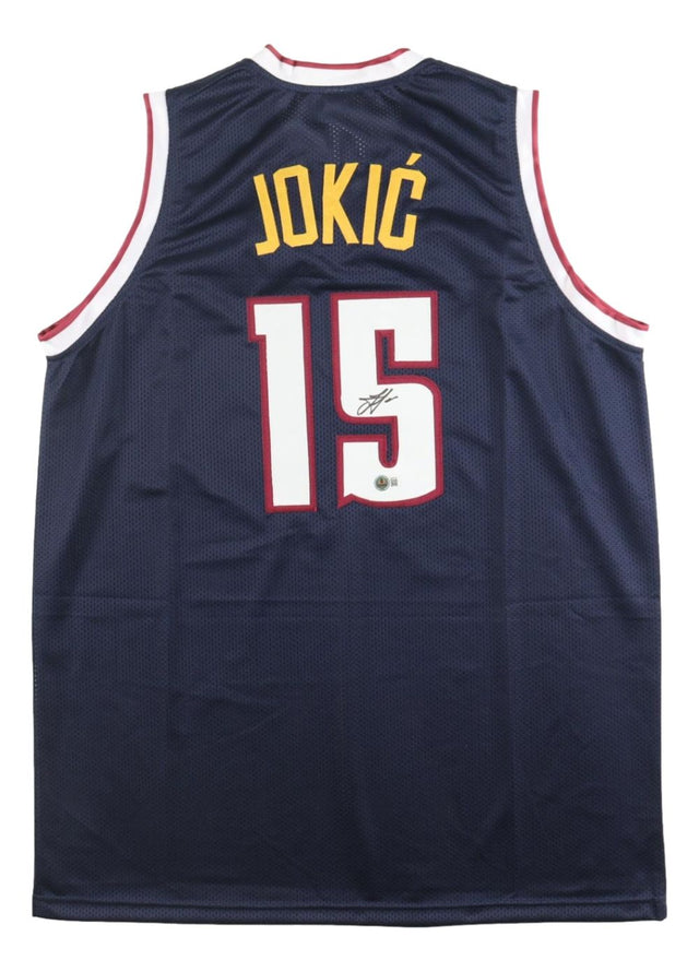 The Sports Integrity Nikola Jokic Denver Signed Navy Basketball Jersey BAS features "JOKIĆ" and number 15 in yellow and white on the back with an autograph below the number and red-white trim.