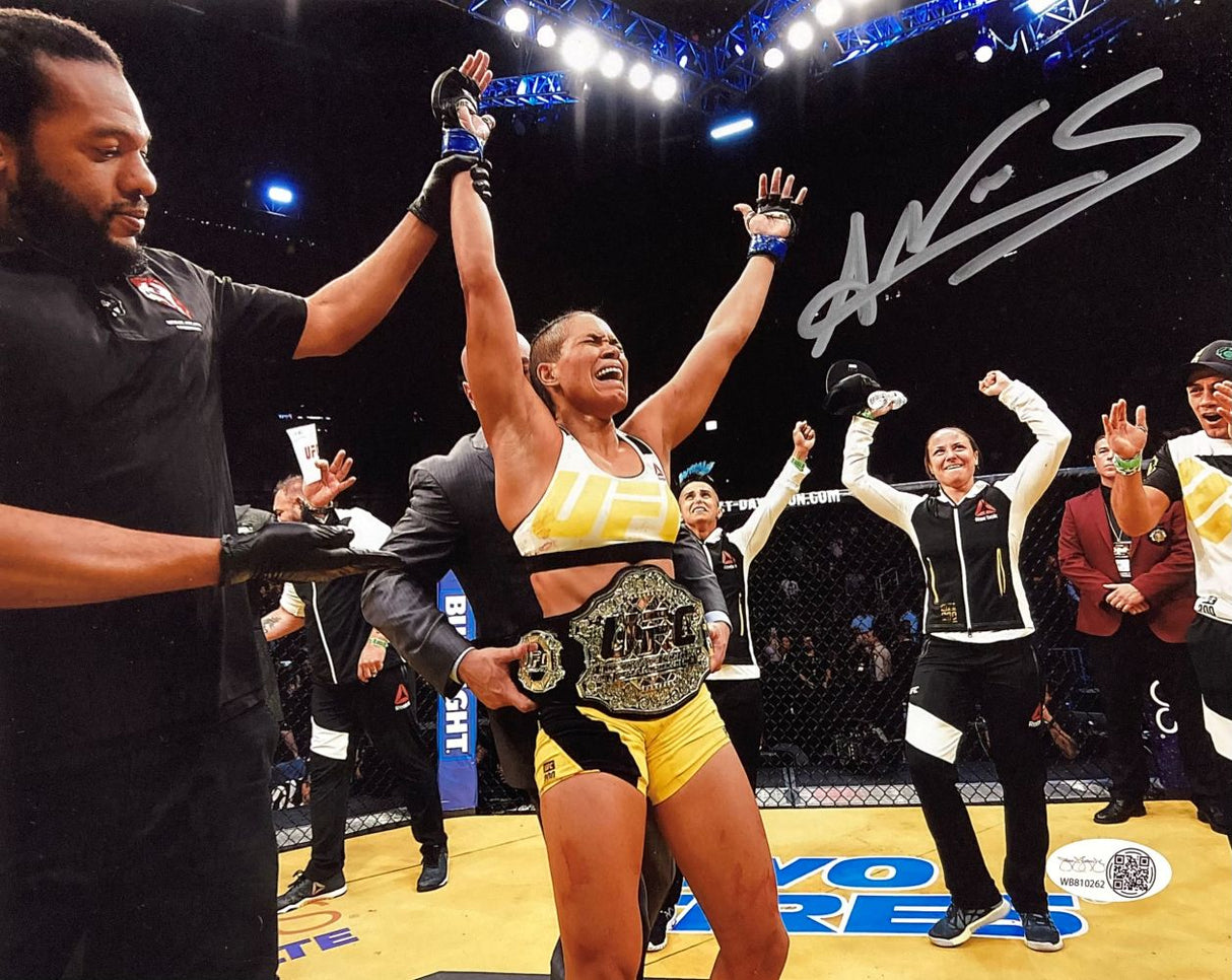 Celebrate Amanda Nunes' victory with this signed 8x10 UFC Championship photo from Sports Integrity, featuring her smiling in the octagon with raised arms and a title belt. The JSA QR hologram and autograph are included.