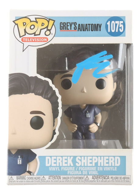 A Patrick Dempsey signed Grey's Anatomy Funko Pop #1075 by Sports Integrity, featuring Derek Shepherd in blue scrubs and a badge, visible through the packaging window.