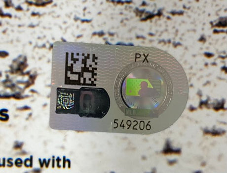 A close-up of a Sports Integrity holographic sticker with QR codes, "PX," and number 549206 on a Paul Skenes Signed 16x20 Pittsburgh Pirates Photo MLB Hologram, set against a textured background with partial printed text.