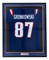 A Sports Integrity Rob Gronkowski New England signed and framed blue football jersey (#87) with PSA/DNA hologram, featuring “GRONKOWSKI” on the back and a display plaque reading “Rob Gronkowski.”.