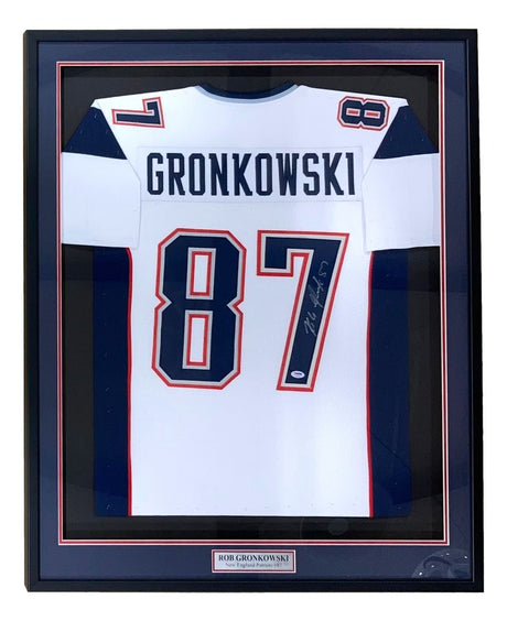 The Sports Integrity Rob Gronkowski New England signed framed white football jersey (#87) features his name, a PSA/DNA hologram, and is displayed in a black frame with a plaque at the bottom.