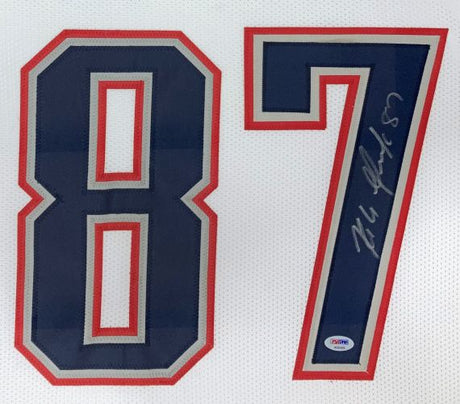 The Sports Integrity Rob Gronkowski New England Signed Framed White Football Jersey features a bold navy number 87 with red and gray outlines, a visible autograph on the 7, and a PSA/DNA hologram authentication sticker.