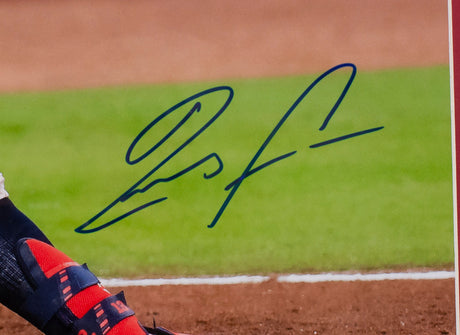 A close-up of a blue autograph on a Ronald Acuna Jr. Signed Framed 16x20 Atlanta Braves Baseball Photo by Sports Integrity, showing part of a player’s red and navy shoe, dirt ground, and green grass in the background.