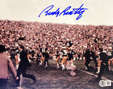 Celebrate Notre Dame with this Rudy Ruettiger Signed 8x10 Photo by Sports Integrity, featuring jersey #45 carried by teammates and a blue autograph at the top. Perfect for any Fighting Irish fan!.