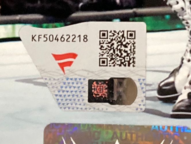A close-up of a tamper-evident authentication sticker with code KF50462218, QR code, red logo, and holographic strip on a Sami Zayn Signed Framed 8x10 WWE Photo by Sports Integrity.