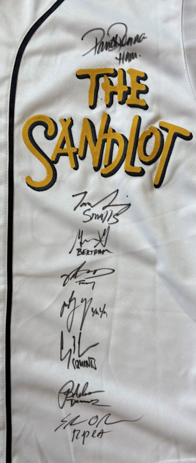 The Sandlot (8) Cast Signed Custom Baseball Jersey by Sports Integrity features bold yellow and black lettering and multiple signatures in black marker vertically arranged down the white jersey.