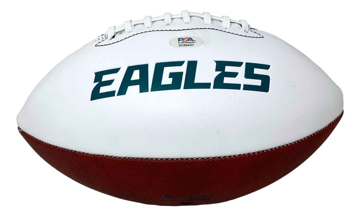 A white and brown Sports Integrity football, signed by Saquon Barkley, features the green EAGLES logo, white laces, and a PSA/DNA authentication sticker near the top.